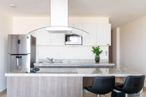 a kitchen with white cabinets and a counter with two chairs at Nuevo Departamento en el Malecón! in Mazatlán