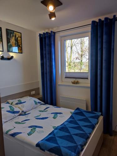 a bedroom with a bed with blue curtains and a window at Leśny Zakątek-Domek Dąb in Parchowo