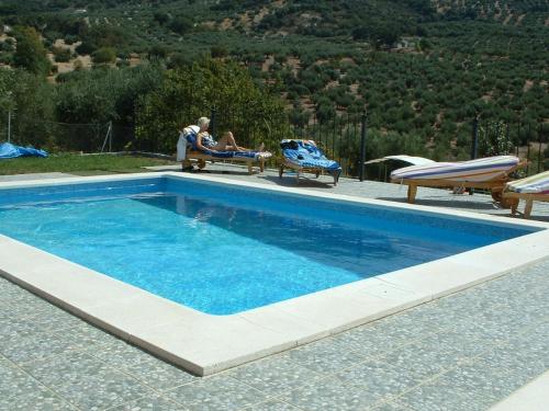 a man sitting on a bench next to a swimming pool at B&B Lasnavillasmm in Montefrío