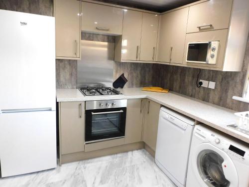 een keuken met witte kasten en een wasmachine en droger bij New & delightful 3 bed house in East Kilbride in Glasgow