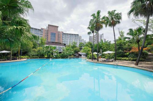 Una gran piscina azul con palmeras y edificios. en Ramada Plaza by Wyndham Chongqing West, en Dazu