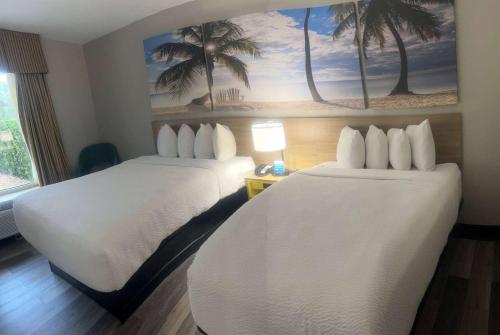 two beds in a hotel room with palm trees on the wall at Days Inn by Wyndham Port Charlotte Town Center in Port Charlotte