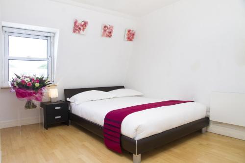 a white bedroom with a bed and a vase of flowers at Holiday Lets London - K in London