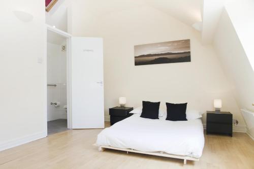 a white bedroom with a white bed with black pillows at Holiday Lets London - K in London