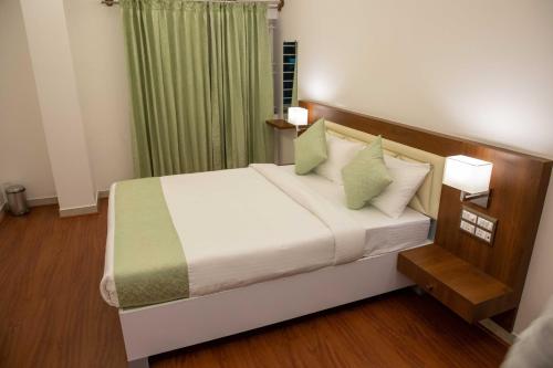 a bedroom with a bed with white sheets and green pillows at PVR Suites off Bannerghatta Road in Bengaluru