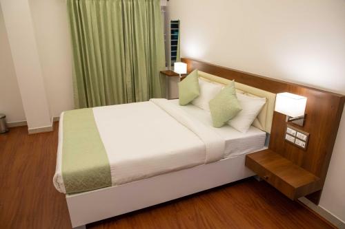 a bedroom with a bed with white sheets and green pillows at PVR Suites off Bannerghatta Road in Bengaluru