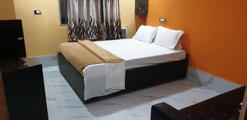 een slaapkamer met een bed met witte lakens en een televisie bij Hotel Eleven in Bhagalpur