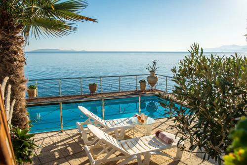 a swimming pool with two chairs and a table and the ocean at Exclusive Seaside Retreat with Shared Pool & Private Beach Access in Palaiokastro