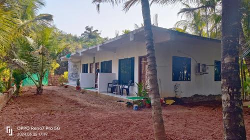 a white house with palm trees in front of it at Makayla Farm Stay in Pernem