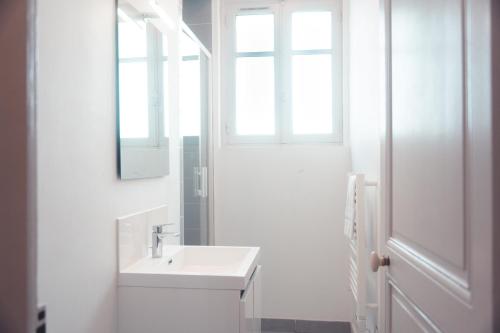 une salle de bain blanche avec un lavabo et un miroir dans l'établissement Le Ronsardien - Appartement calme et confortable, à Tours