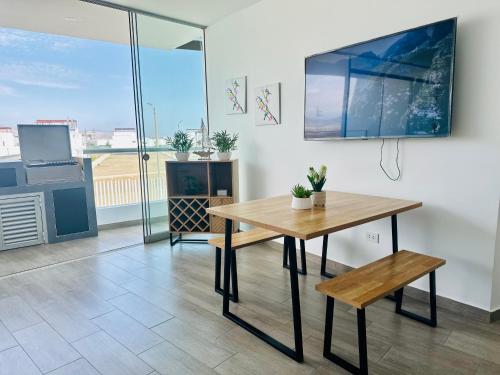 une table et un banc dans une chambre avec une grande fenêtre dans l'établissement ¡A 3 minutos de la Playa! Hermoso Departamento de Estreno con Piscina y Parrilla, à Asia