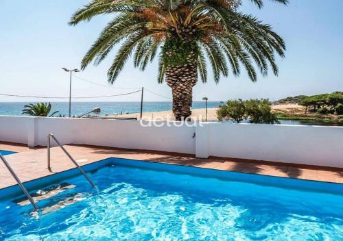 uma piscina com uma palmeira e o oceano em BEACH PALACE CB08 em Platja d'Aro