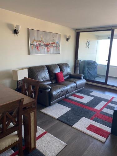a living room with a leather couch and a table at Departamentos Mednav Montemar & Spa in Concón