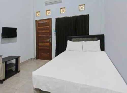 a bedroom with a large white bed and a television at Wisma Dhana Syariah in Praya