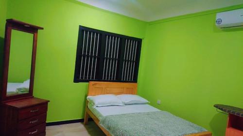 a green bedroom with a bed and a mirror at LIllyPo in Point Pedro
