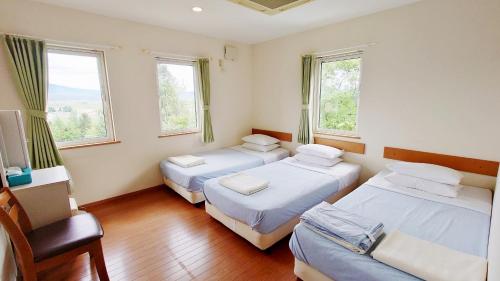 a room with three beds and a chair and two windows at Pension and Restaurant La Collina in Nakafurano
