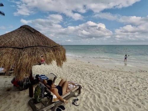 two people laying on a beach under a straw umbrella at Apartamento de lujo en playa in Playa del Carmen
