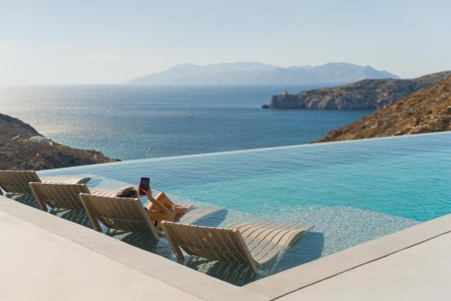 a woman laying in chairs next to a swimming pool at On The Rocks Villas Ios in Ios Chora