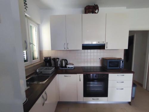 eine Küche mit weißen Schränken, einer Spüle und einer Mikrowelle in der Unterkunft Apartman Elephant in Postira