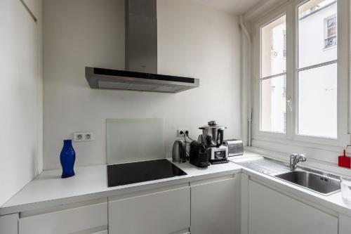 une cuisine blanche avec un évier et un micro-ondes dans l'établissement Appartement Palido - Welkeys, à Paris