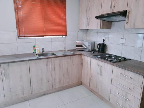 cocina con armarios de madera, fregadero y microondas en Reutlwane Gardens Apartments en Secunda