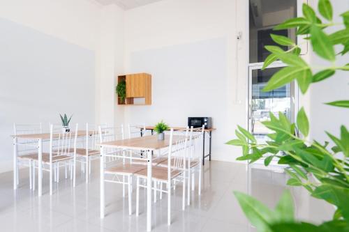 une salle à manger avec des tables blanches, des chaises et des plantes dans l'établissement Hatyai Humble Home 03, à Hat Yai