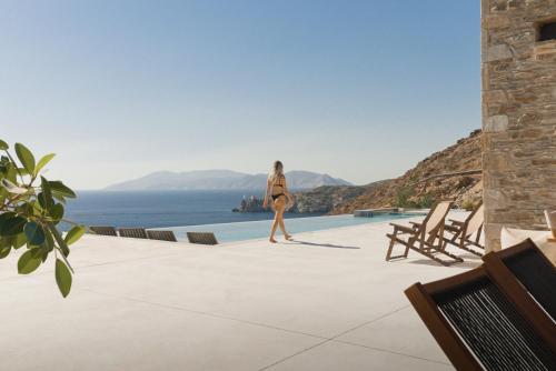 a woman walking on a patio looking out at the ocean at On The Rocks Villas Ios in Ios Chora