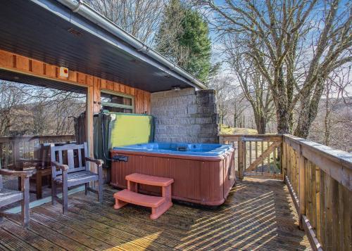 a hot tub on a deck with a chair and a table at Wildside Highland Lodges in Whitebridge