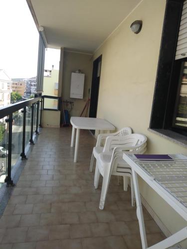 Un balcón con mesas blancas y sillas en un edificio en Appartamento Gianna en Alghero