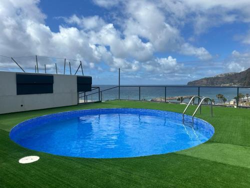 a large blue swimming pool on a green field with the ocean at Flag Hotel Madeira - Ribeira Brava in Ribeira Brava