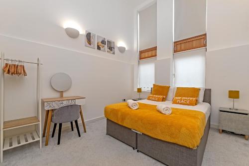a bedroom with a bed with orange sheets and a desk at Stylish 2 bedroom apartment, 2 bathrooms, free parking for all guest, wifi, Sky, Netflix, walking distance to city centre, sleeps 5, outside patio space, ground floor in Milton Keynes