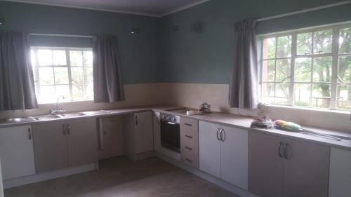a kitchen with white cabinets and two windows at Two Bed Two Bath Cottage in Bulawayo