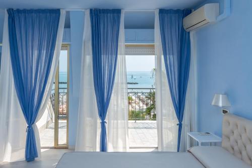 a bedroom with blue curtains and a bed and a large window at Hotel Dino in San Benedetto del Tronto