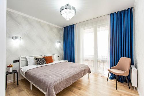 a bedroom with a bed with blue curtains and a chair at Alpine serenity deLuxe apartment with MOUNTAIN views near the ADK shopping center and Sairan METRO station in Almaty