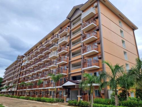 an apartment building with palm trees in front of it at DELUXE ROOM Queen Bed & Sofa Bed with Balcony and Swimming Pool at PPS in Puerto Princesa City