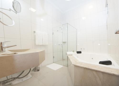 a white bathroom with a tub and a shower at Gold Hotel Navirai in Naviraí