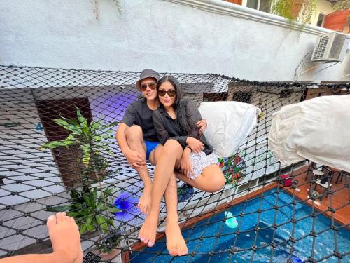 two people sitting on a fence next to a swimming pool at Hostelito Hotel in Cozumel