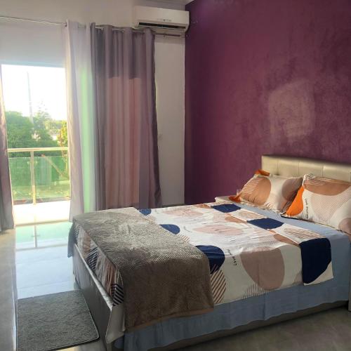um quarto com uma cama com uma parede roxa em Guest House Meg Alfa em Luanda