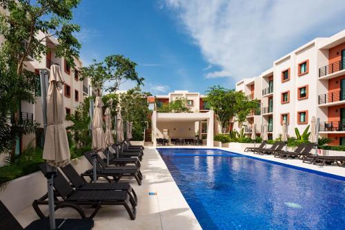 a swimming pool with chaise lounge chairs and umbrellas at Acogedor apartamento en Ombu Huayacan in Cancún