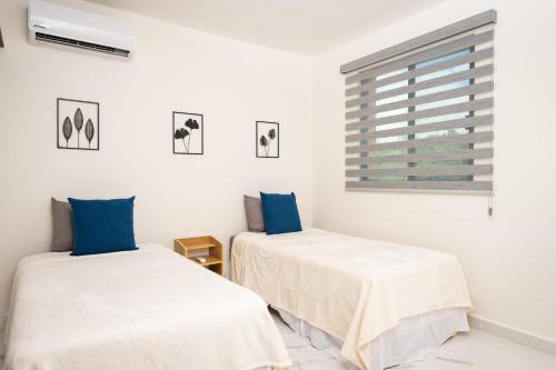 two beds in a white room with blue pillows at Acogedor apartamento en Ombu Huayacan in Cancún