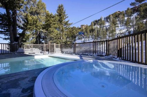 une piscine avec une clôture et un bain à remous dans l'établissement Arc 1950 - Appt 2CH - 6 pers - Rés 5* luxe - Piscine, sauna, hamman, jacuzzi - Classé 5 cristaux Paradiski, à Arc 1950