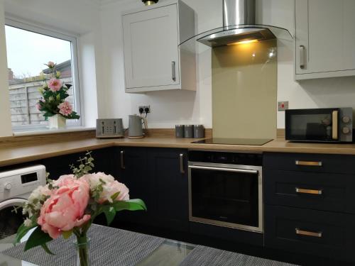 uma cozinha com armários brancos e um vaso de flores em Polaris House - sleeps 6, driveway, garden em Crewe