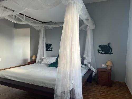 1 dormitorio con cama con dosel y cortinas blancas en Appartement Melissa97- Bât4 Spacieux à Dzamandzar en Nosy Be