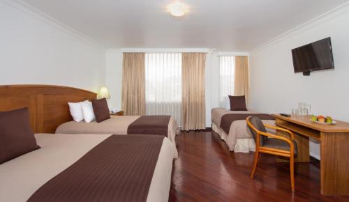 um quarto de hotel com duas camas e uma secretária em Hotel Tourblanche em Quito