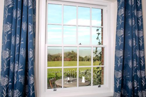 a window with blue curtains and a table with a view at Fort Victoria Cottages - Sea View Cottage in Yarmouth