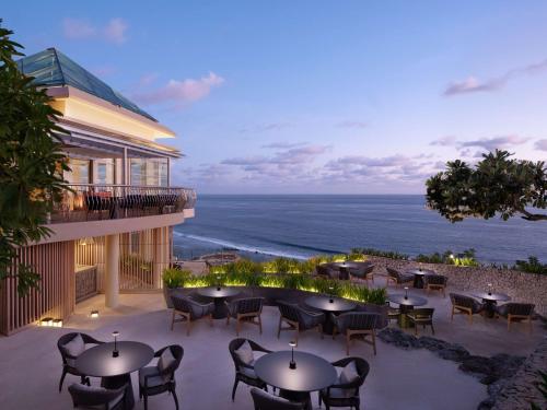 a patio with tables and chairs and the ocean at Umana Bali, LXR Hotels & Resorts in Uluwatu