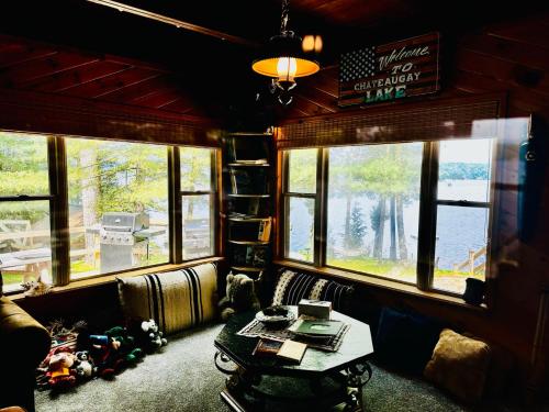 una sala de estar con una mesa y ventanas en un tren en Well-appointed ADK cabin directly on 106’ water!, 