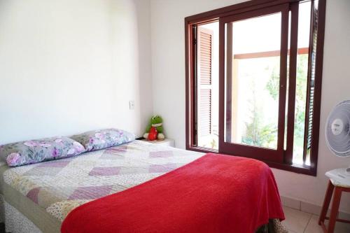 - une chambre avec un lit doté d'une couverture rouge et d'une fenêtre dans l'établissement Casa aconchegante, à Passo de Torres