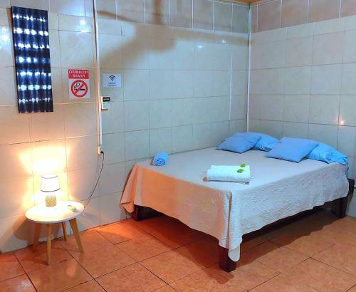 Habitación pequeña con cama y mesa con lámpara. en Hostel del Pacífico, en Puntarenas