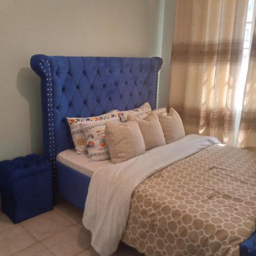 uma cama com uma cabeceira azul com almofadas em Verona Apartments em Thika